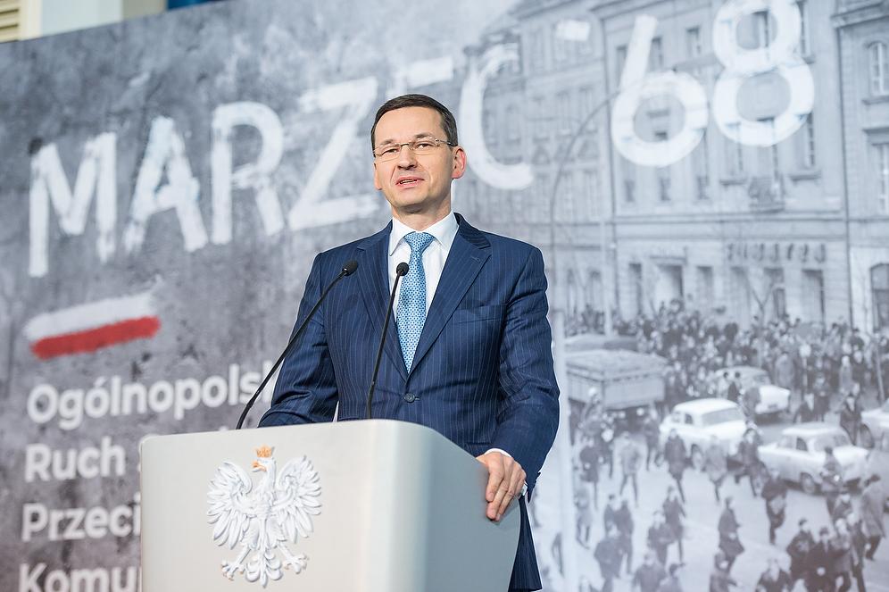 Premier Mateusz Morawiecki przy mównicy, a w tle napis "Marzec '68".