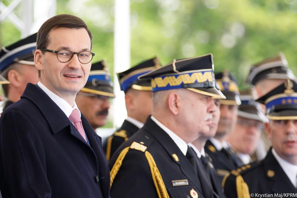 Premier Mateusz Morawiecki stoi podczas uroczystości, obok oficerowie straży.