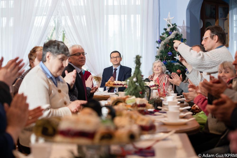 Premier Mateusz Morawiecki przy stole z seniorami.