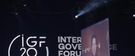 Szczyt Cyfrowy ONZ – IGF 2021. Duże logo IGF, obok ekran, na którym wyświetlany jest rozmówca połączony online. Fot. PAP