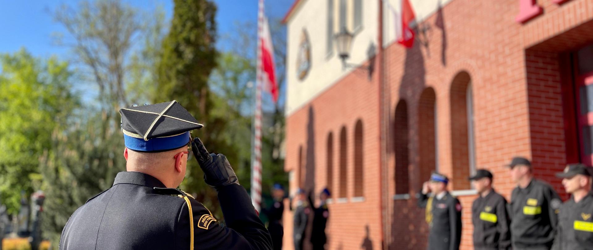 Moment podniesienia Flagi Państwowej Rzeczypospolitej Polskiej. Strażacy w czasie uroczystej zbiórki oddają honor.