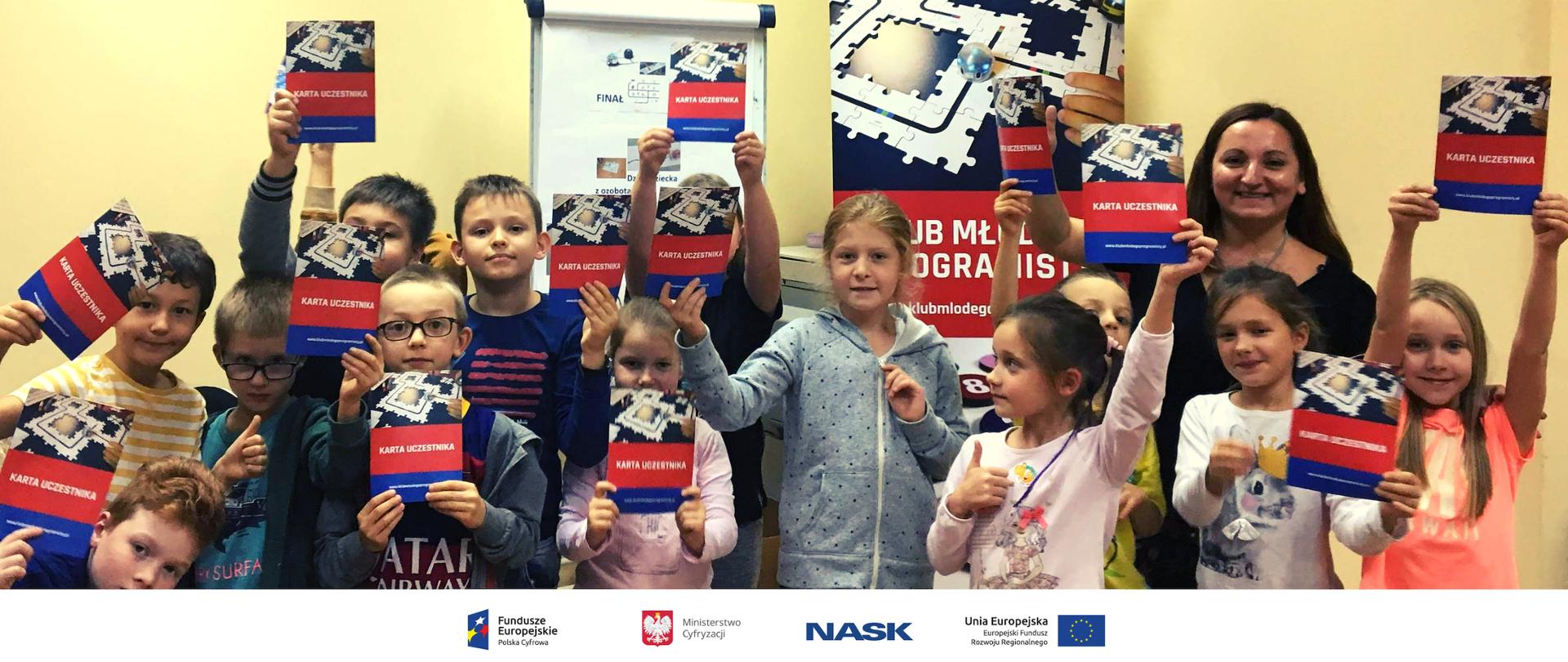 Kilkanaścioro dzieci trzyma publikację "Kartę uczestnika Klubu Młodego Programisty".