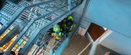 Strażacy rozwijają linię gaśniczą na klatce schodowej