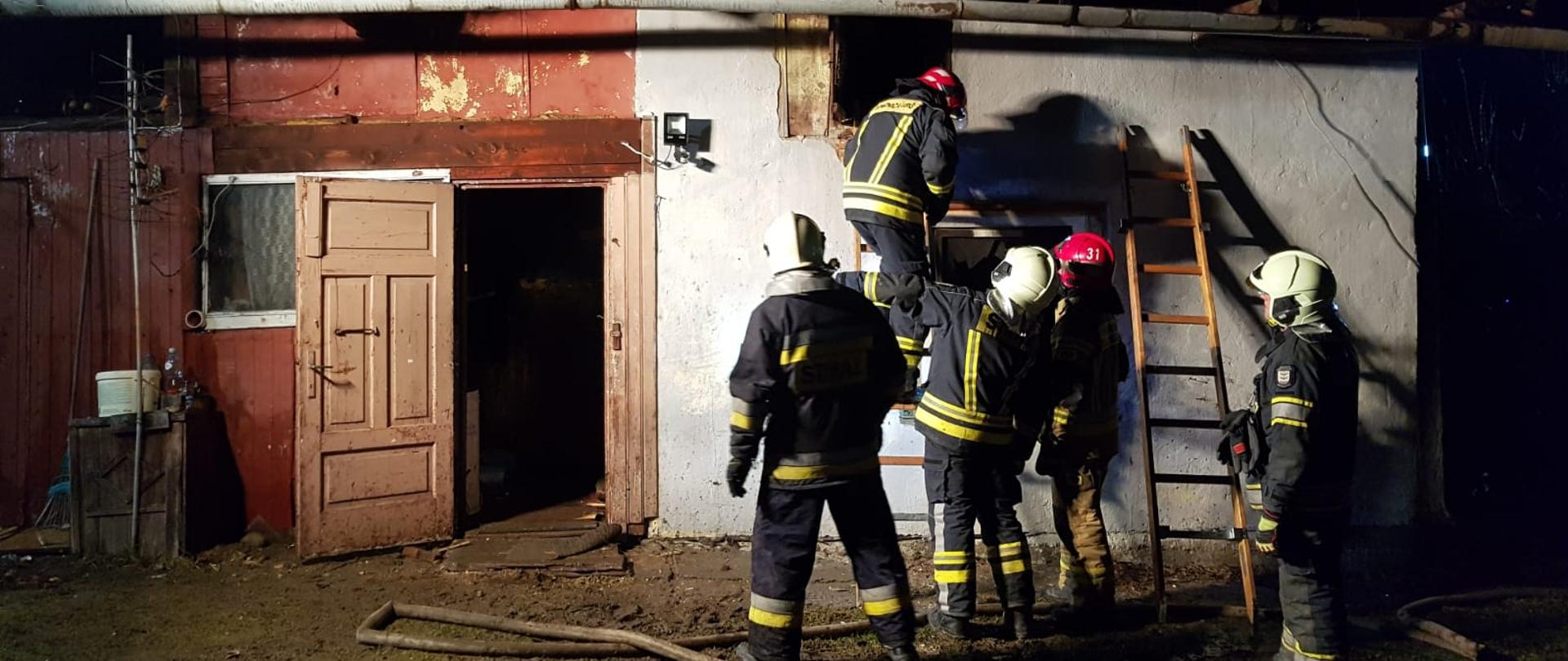 Zdjęcie przedstawia strażaków pracujących przed budynkiem, w którym był pożar. 