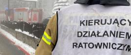Na zdjęciu widać strażaka dowódcę prowadzącego akcję. Na plecach dowódcy znajduje się kamizelka z napisem Kierujący Działaniem Ratowniczym. 