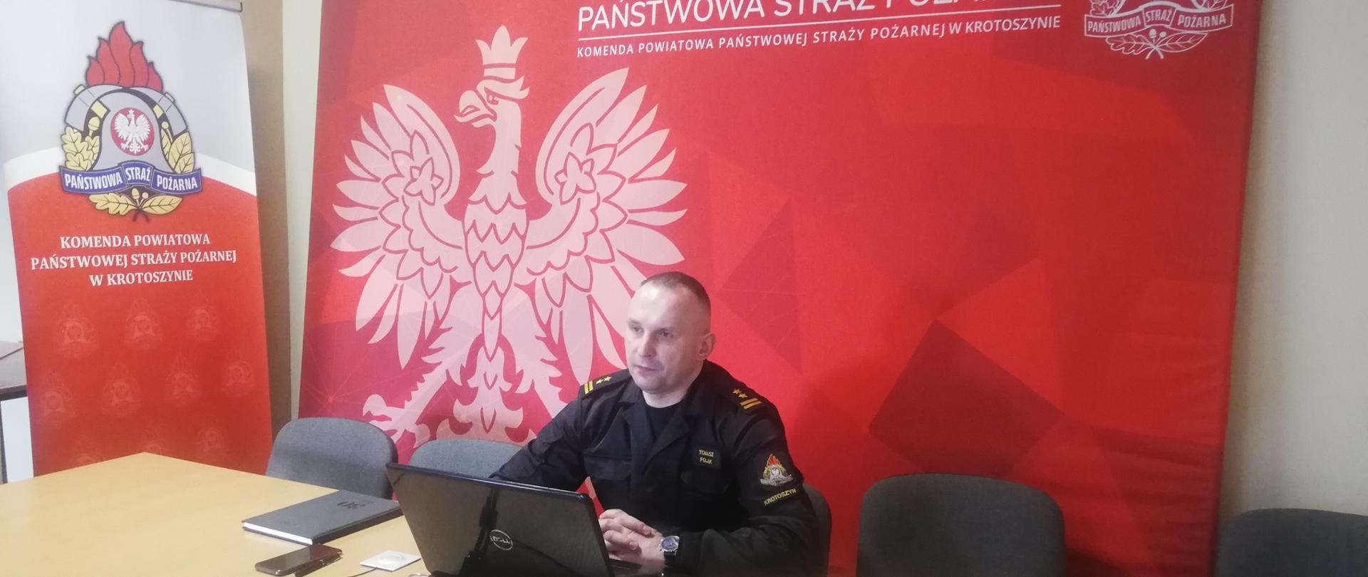 Zdjęcie przedstawia komendanta powiatowego PSP w Krotoszynie, który siedzi przy stole z laptopem i przedstawia materiał z działalności JOP za rok 2021