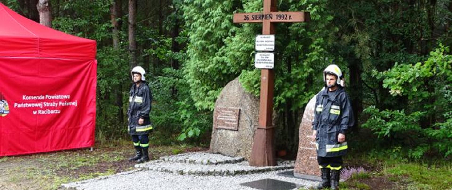 Strażacy w ubraniach specjalnych stojący po obu stronach pomnika upamiętniającego ofiary pożaru w Kuźni Raciborskiej 