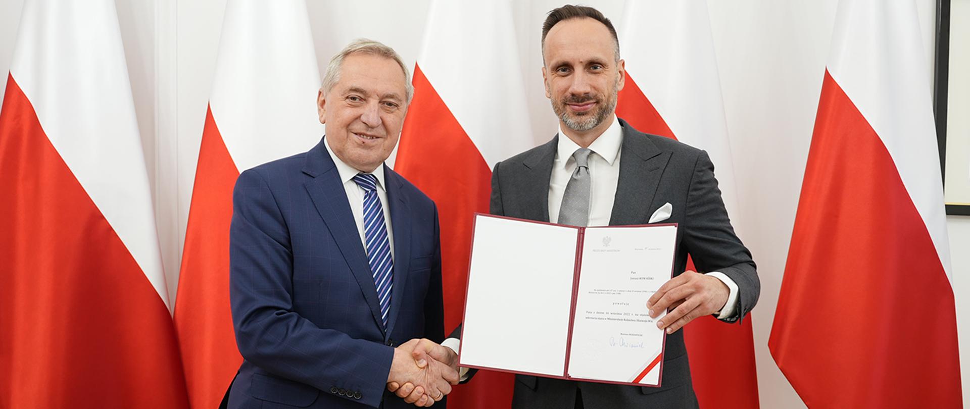 wicepremier Henryk Kowalczyk i sekretarz stanu Janusz Kowalski stojący na tle polskich flag