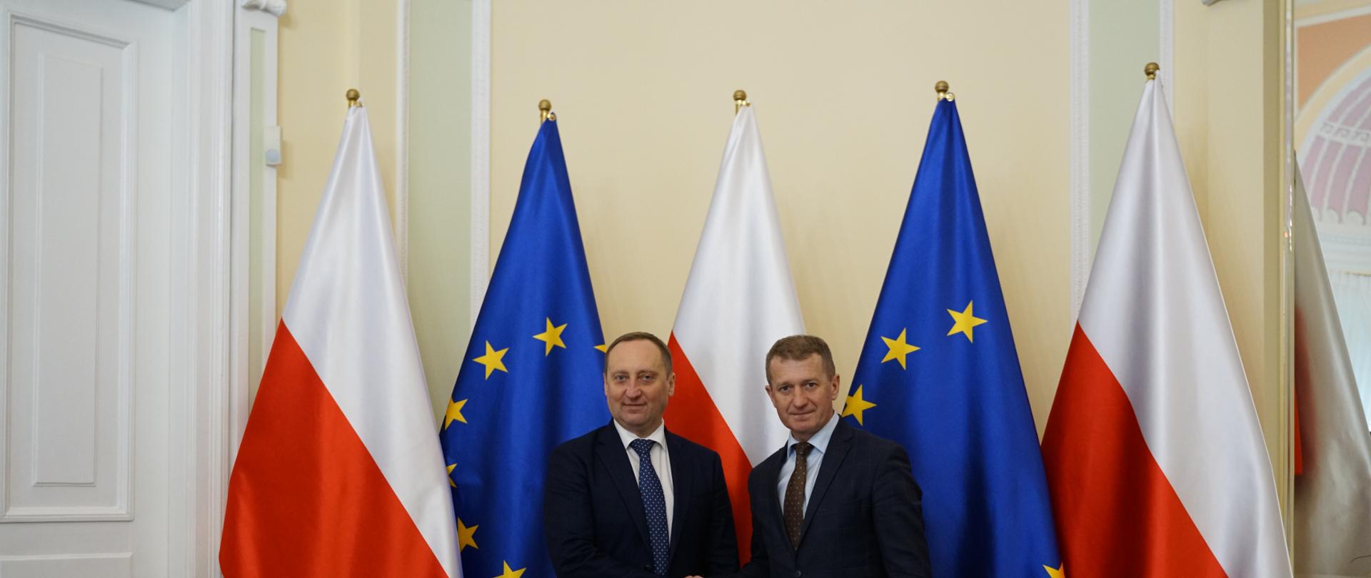 two men shaking hands with the flags of Poland and European Union in the background