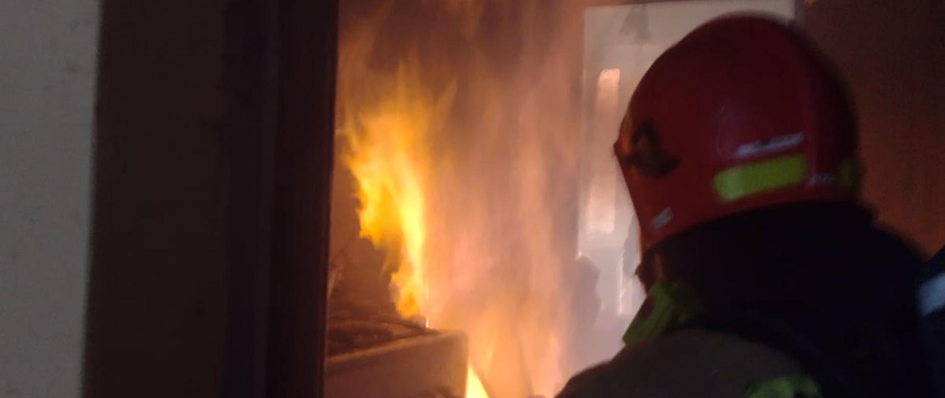 Strażak wchodzi do płonącego mieszkania.