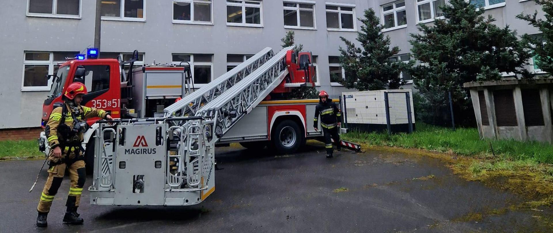 Na zdjęciu strażak podczas rozkładania mechanicznej drabiny pożarniczej stojący w umundurowaniu specjalnym wyposażony w hełm i aparat powietrzny. Scena podczas prowadzonych ćwiczeń.