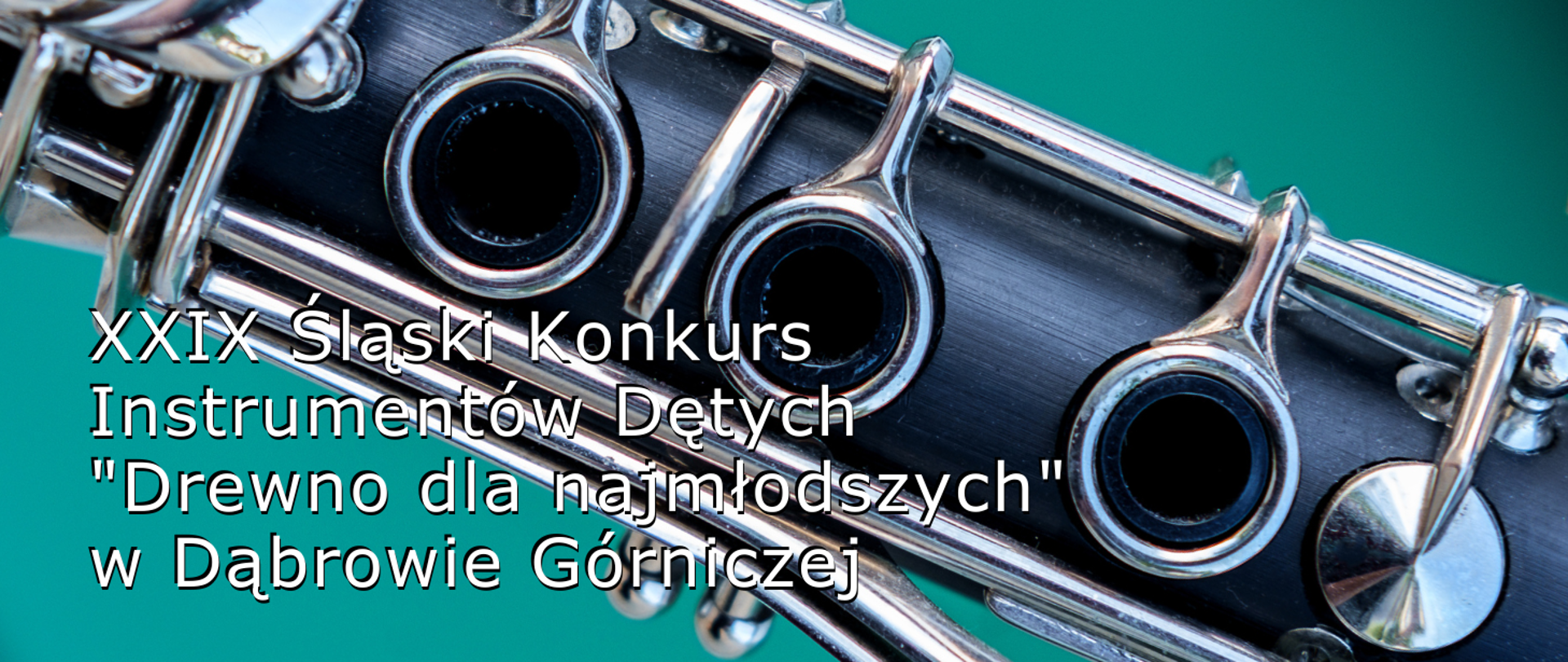 Kolorowe zdjęcie środkowej części klarnetu z klapkami, znajdującego się na turkusowym tle. W lewym dolnym rogu biały napis XXIX Śląski Konkurs Instrumentów Dętych "Drewno dla najmłodszych" w Dąbrowie Górniczej