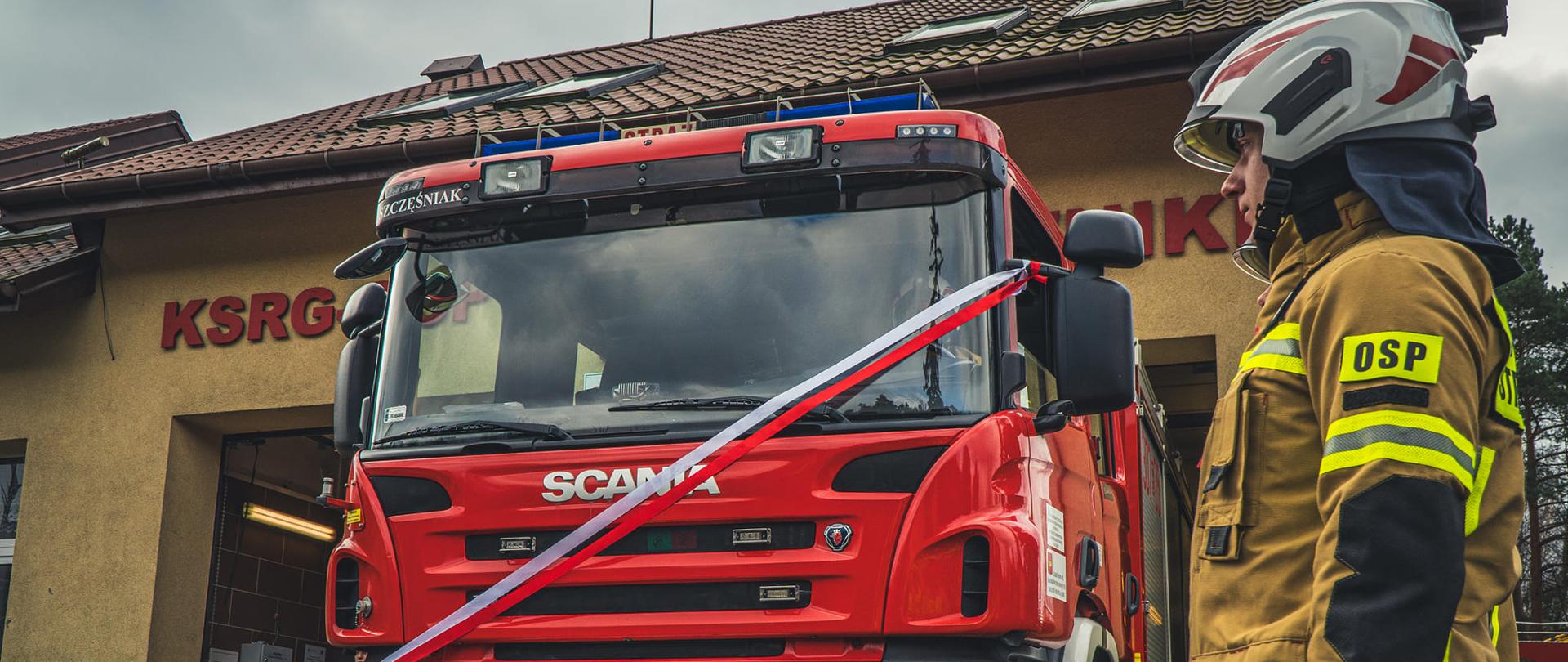 Strażak stojący na baczność przy samochodzie ratowniczo gaśniczym