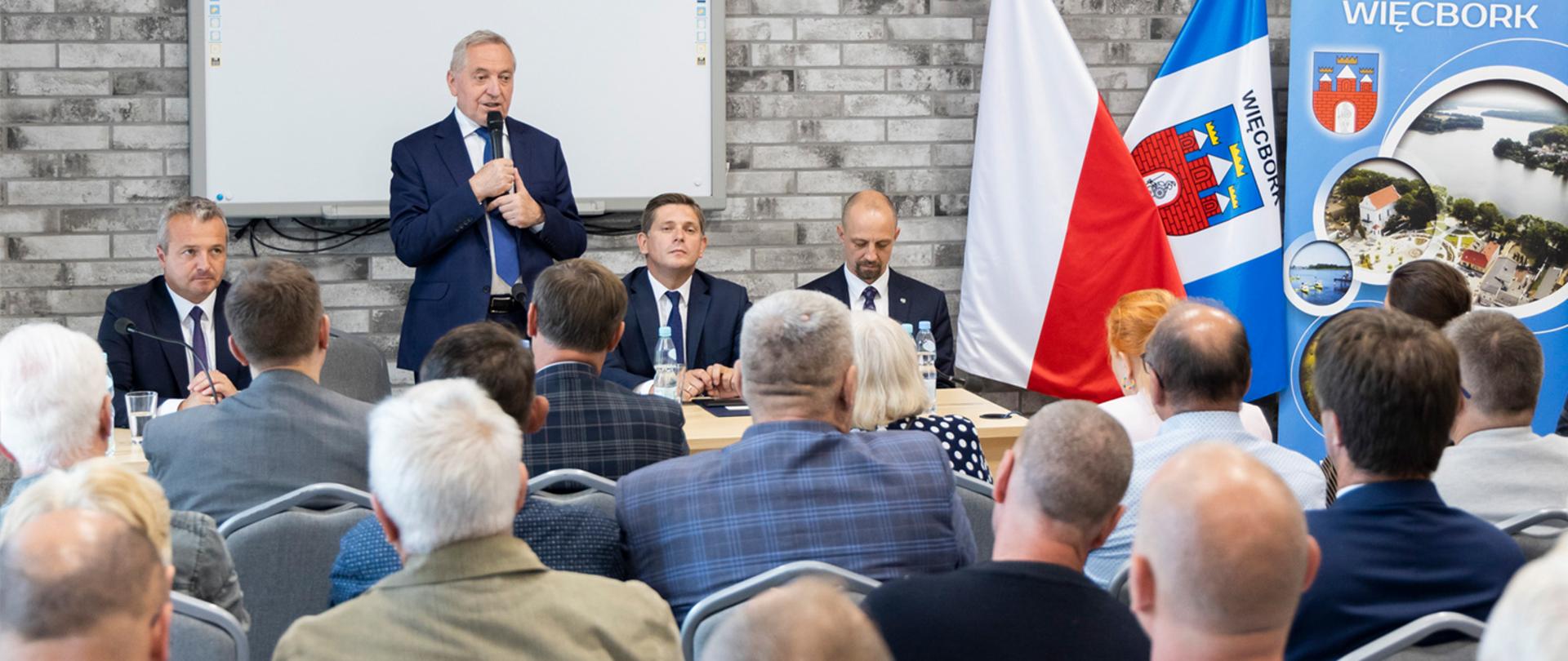 wicepremier Henryk Kowalczyk, stojący z mikrofonem w dłoniach za stołem prezydialnym