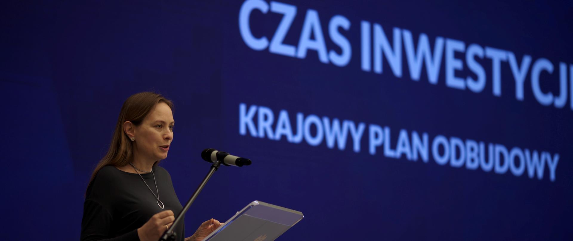 Minister Katarzyna Pełczyńska-Nałęcz stoi z lewej stronie przy pulpicie i mówi do mikrofonu.