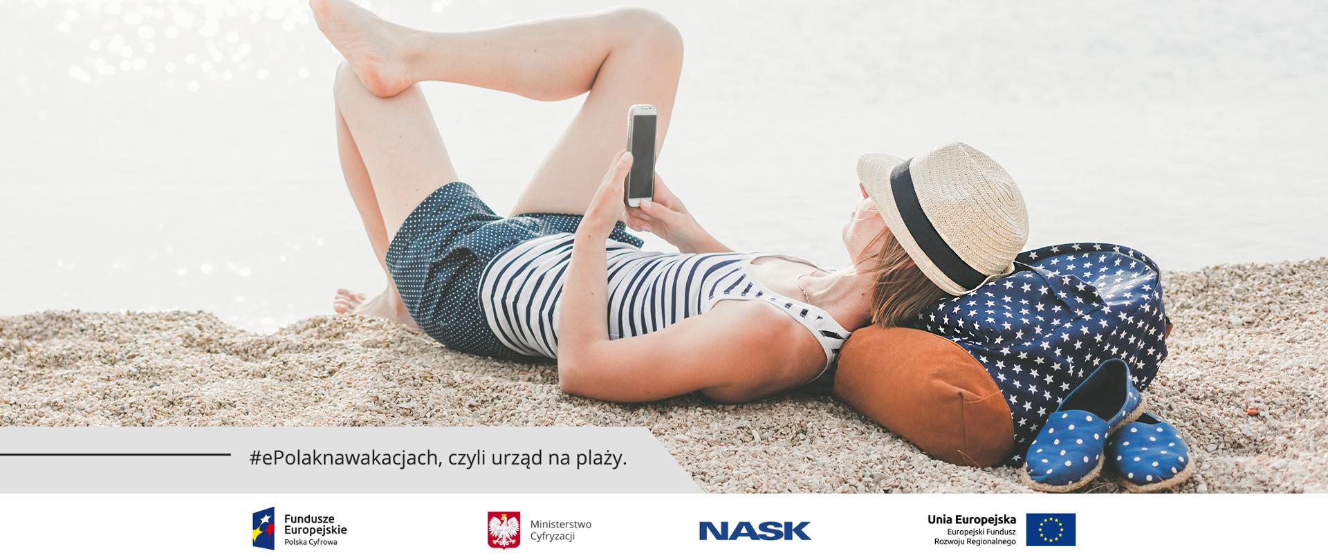 Leżąca na plaży kobieta ze smartfonem w dłoni.