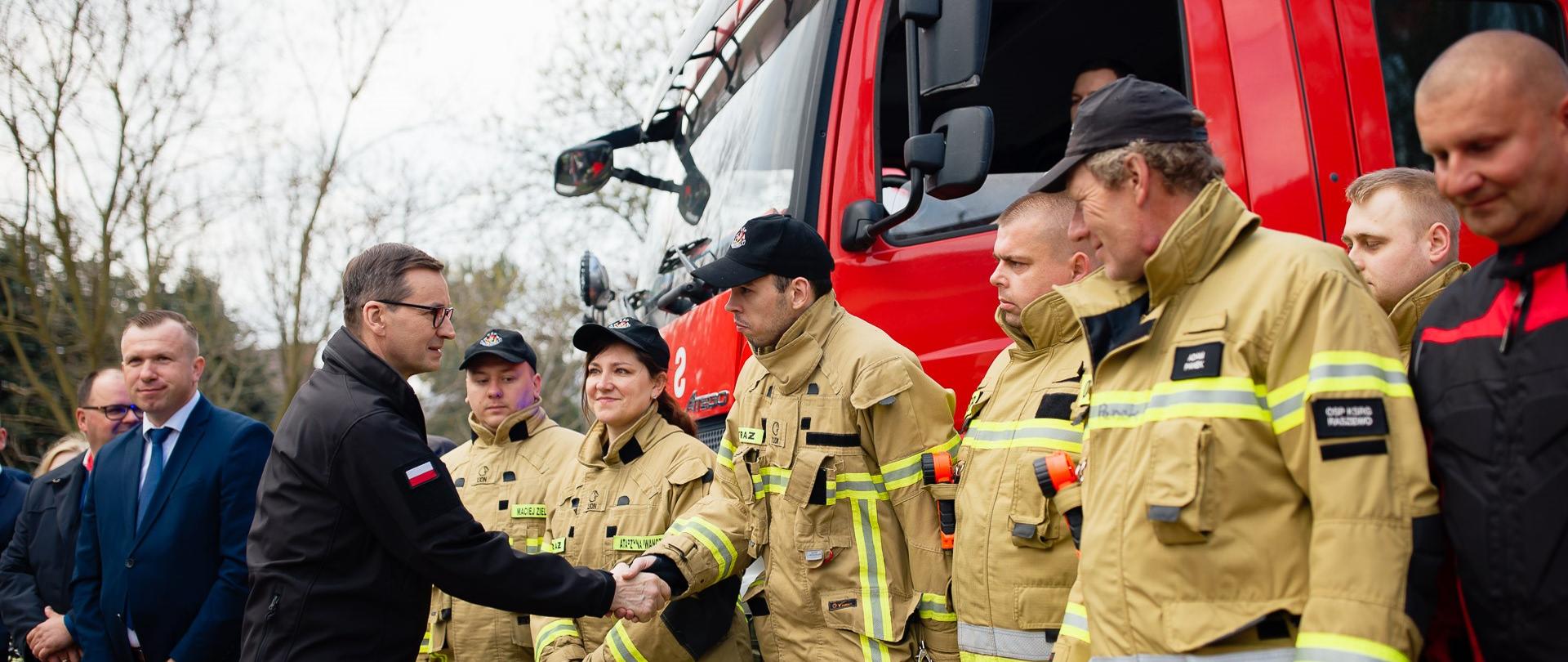 Premier Mateusz Morawiecki wita się ze strażakami.