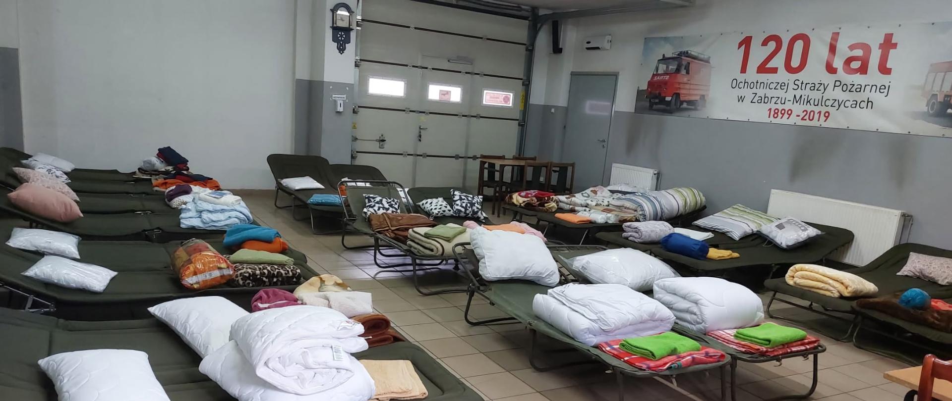 Łóżka polowe z przygotowanymi poduszkami i pościelami na świetlicy jednostki Ochotniczej Straży Pożarnej w Zabrzu Mikulczycach.