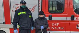 Zdjęcie przedstawia druha OSP w Dunajku z osobą starszą na tle pojazdu pożarniczego, którym została dowieziona do punktu szczepień