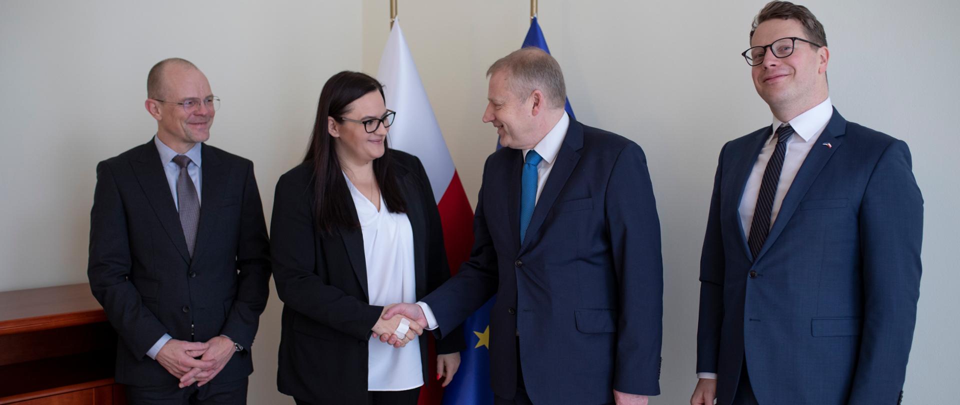 Na zdjęciu stoją cztery osoby - trzech mężczyzn i kobieta. Minister Jarosińska podaje rękę Rainerowi Saks, sekretarzowi generalnemu Ministerstwa Spraw Zagranicznych Estonii.