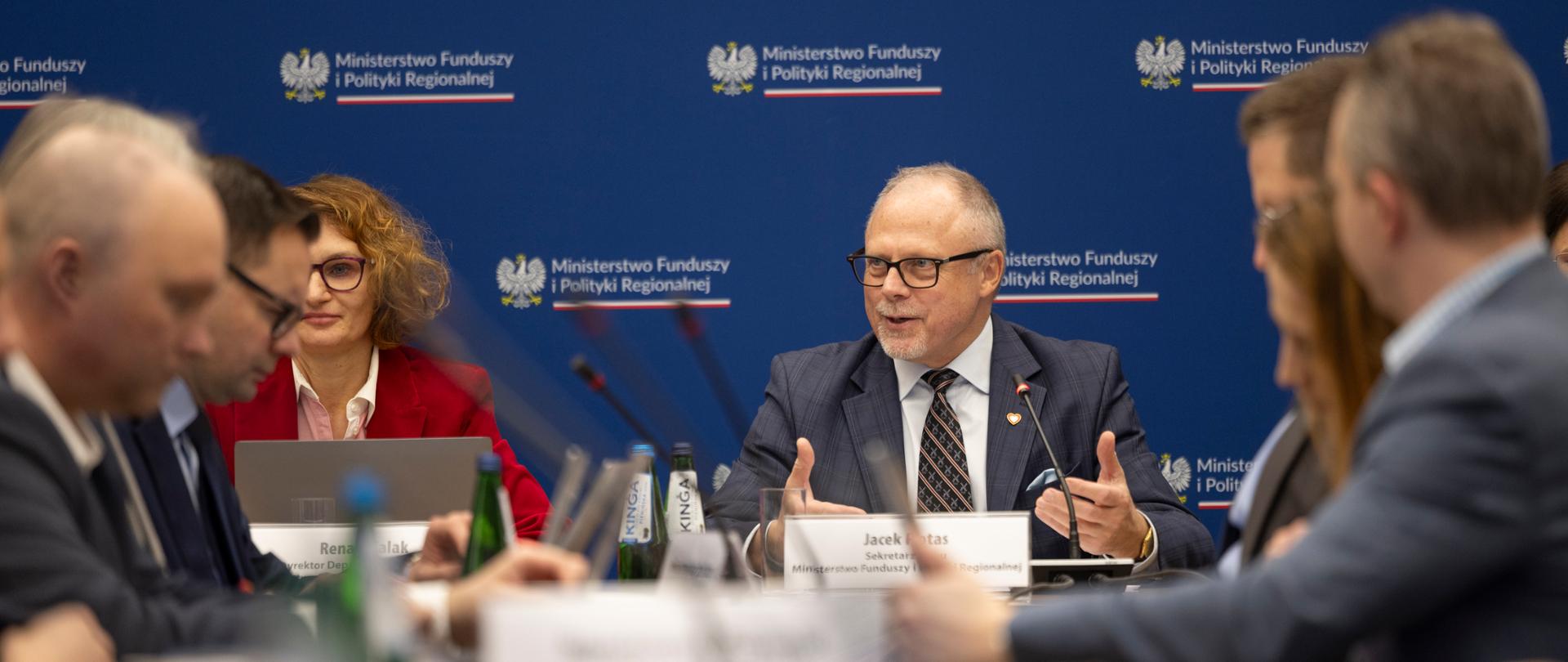 Wiceminister Jacek Protas wśród osób osób siedzących przy stołach