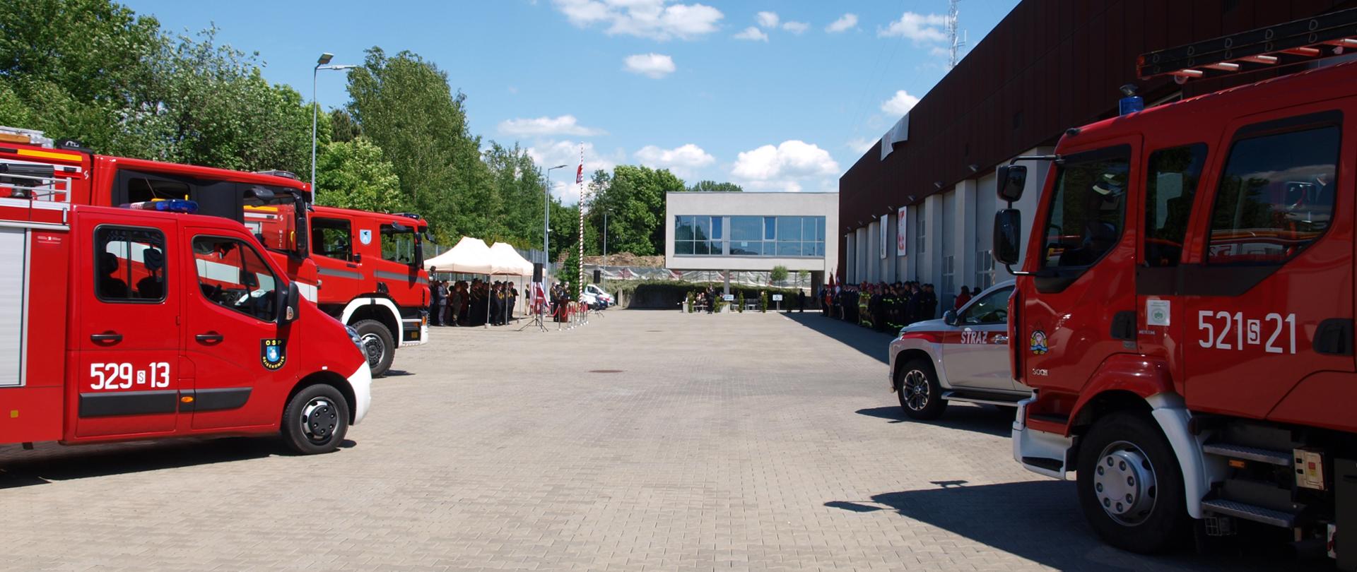 Zdjęcie przedstawia plac wewnętrzny KM PSP w Mysłowicach wraz z samochodami strażackimi oraz strażakami uczestniczącymi w obchodach. 