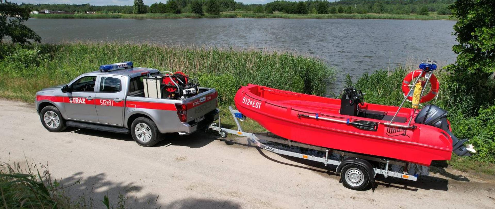 Na zdjęciu widoczny samochód ratowniczy z łodzią ratunkową na tle zalewu. 