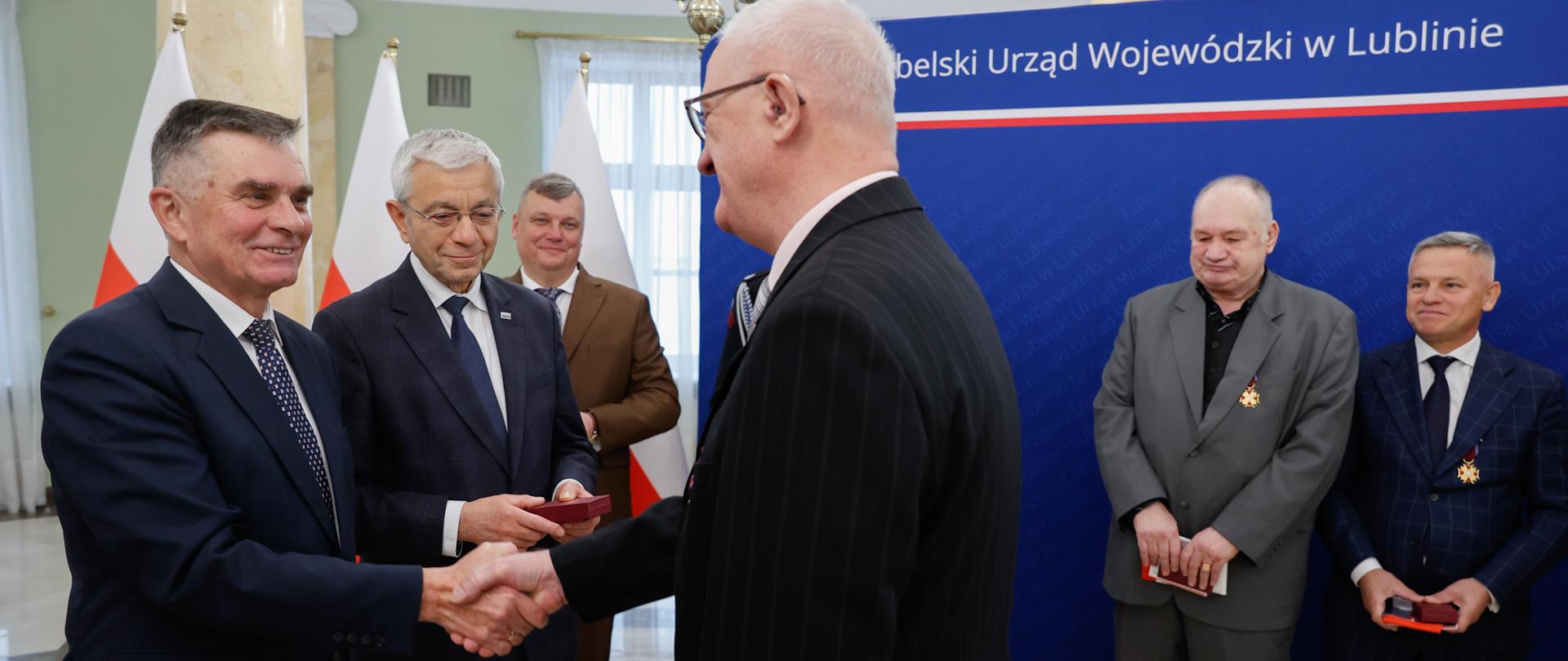 Wojewoda lubelski Lech Sprawka gratuluje mężczyźnie otrzymanego odznaczenia.