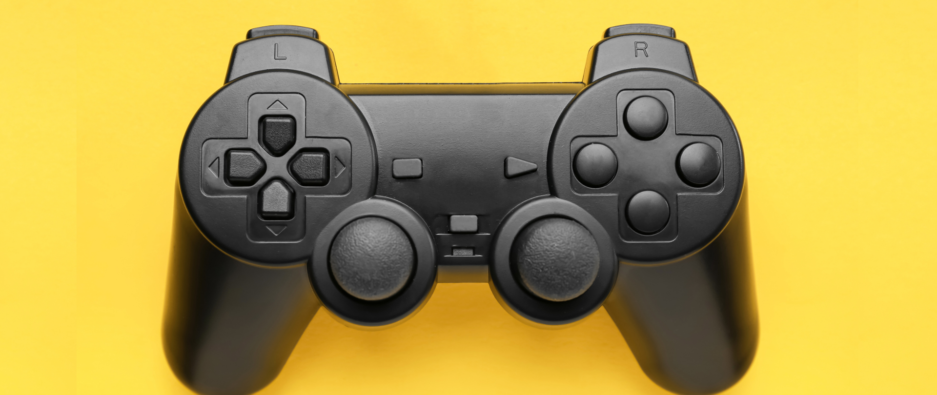 Grafika przedstawia na żółtym tle umieszczonego czarnego pada do gry na konsoli.