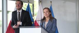 Minister funduszy i polityki regionalnej Katarzyna Pełczyńska-Nałęcz stoi przy mównicy, po jej prawej stronie stoi wiceminister Jan Szyszko, za ich plecami flagi Polski i UE