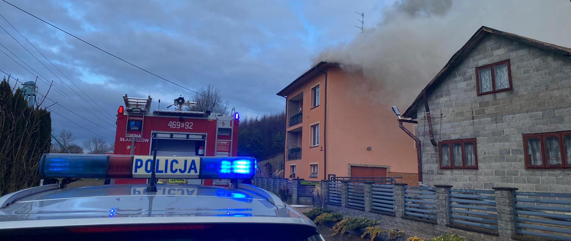 Na zdjęciu widoczy rozwinięty pożar poddasza w domu jednorodzinnego obo zapakowane samochody gaśnicze oraz radiowóz Polcji
