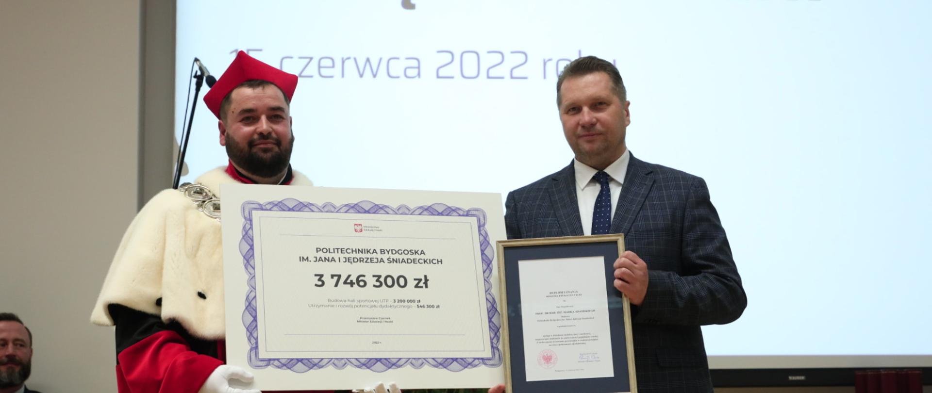 Minister prezentuje symboliczny czek na kwotę 3 746 300 zł.