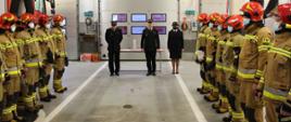 Zdjęcie przedstawia strażaków podczas uroczystej zmiany służy i wręczenia podziękować oraz awansów.
W tle wnętrze garażu JRG.
