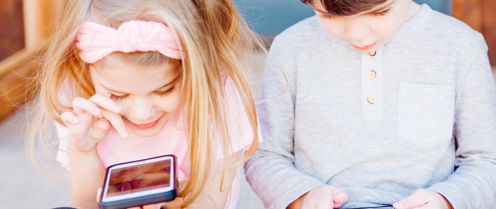 Mała dziewczynka i chłopiec bawiący się smartfonami