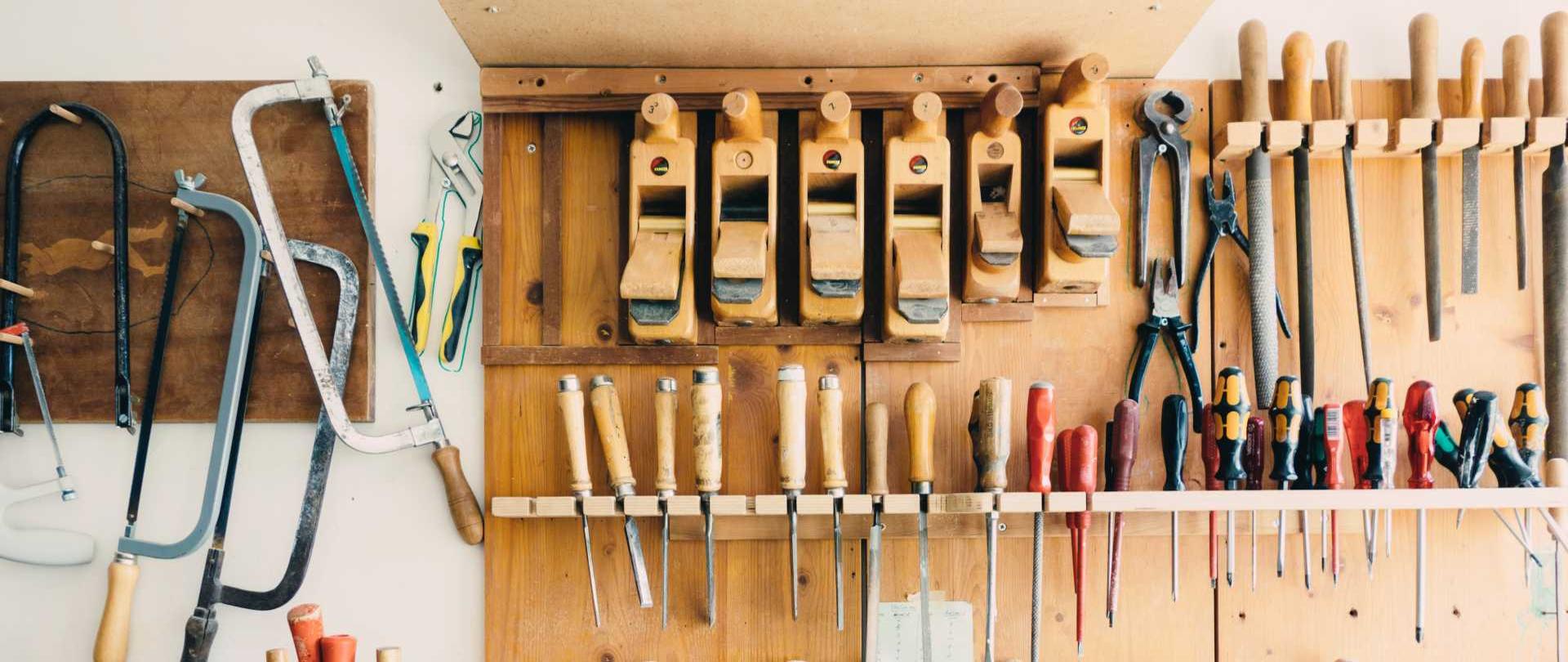 fotografia przedstawia warsztat stolarski z narzędziami stolarskimi zawieszonymi na drewnianych półkach