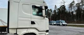 Ciężarówka zatrzymana przez opatowskich inspektorów świętokrzyskiej Inspekcji Transportu Drogowego na DK74. Po lewej pojazd ciężarowy, po prawej w oddali dwa inspekcyjne furgony.