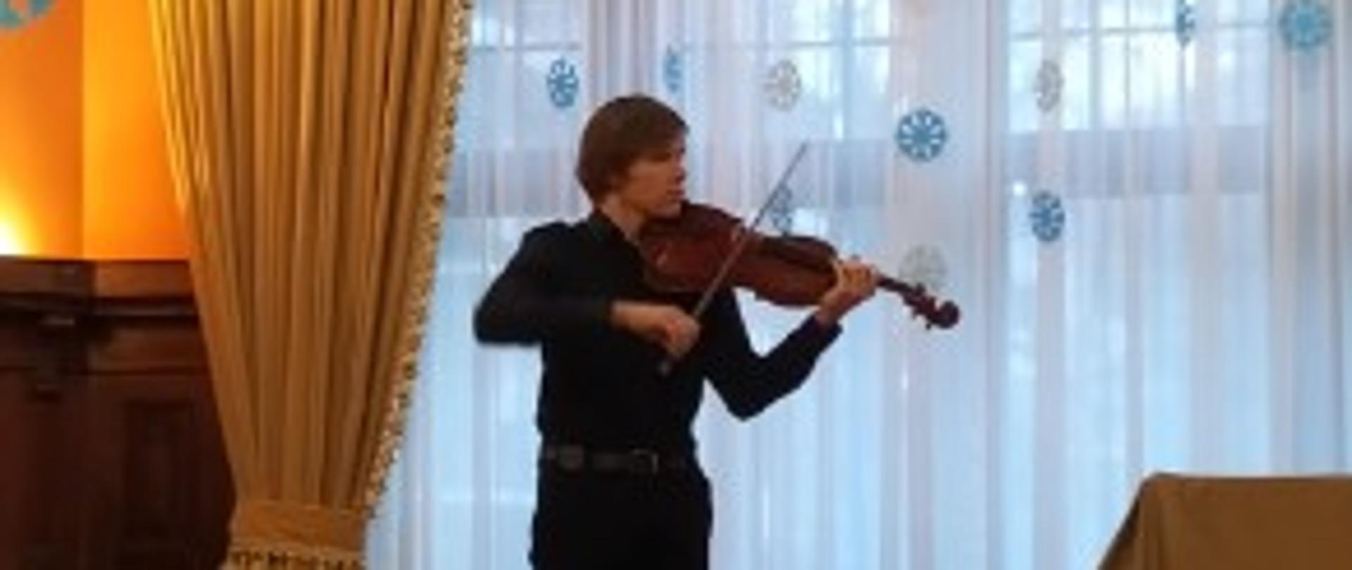 Na zdjęciu uczeń gra na skrzypcach, w tle okno i dekoracja