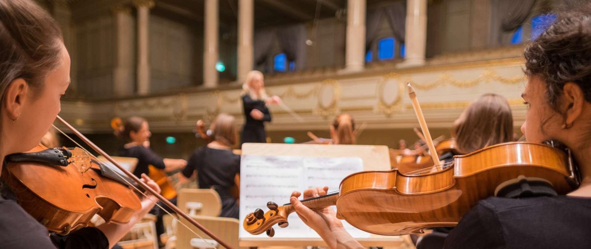 fotografia przedstawia koncert orkiestry smyczkowej na deskach sceny sali koncertowej