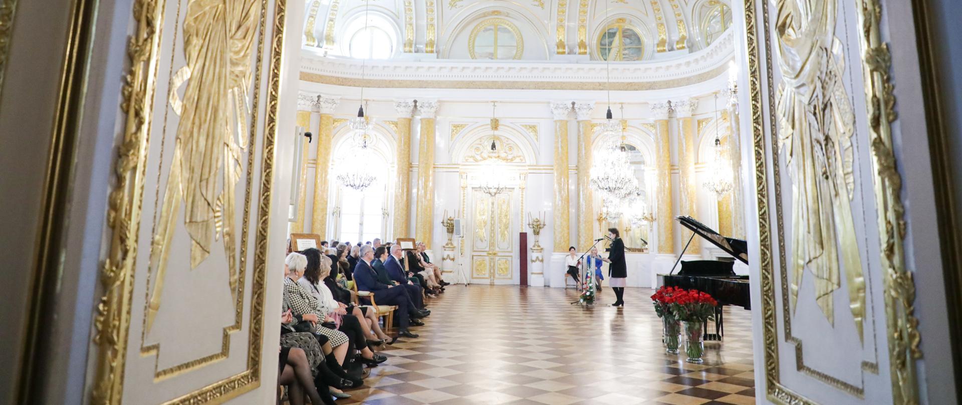 Kolorowe zdjęcie przedstawiające salę balową na Zamku Królewskim w Warszawie oraz zgromadzonych w sali wyróżnionych nauczycieli oraz Panią Wiceminister Wandę Zwinogrodzką.