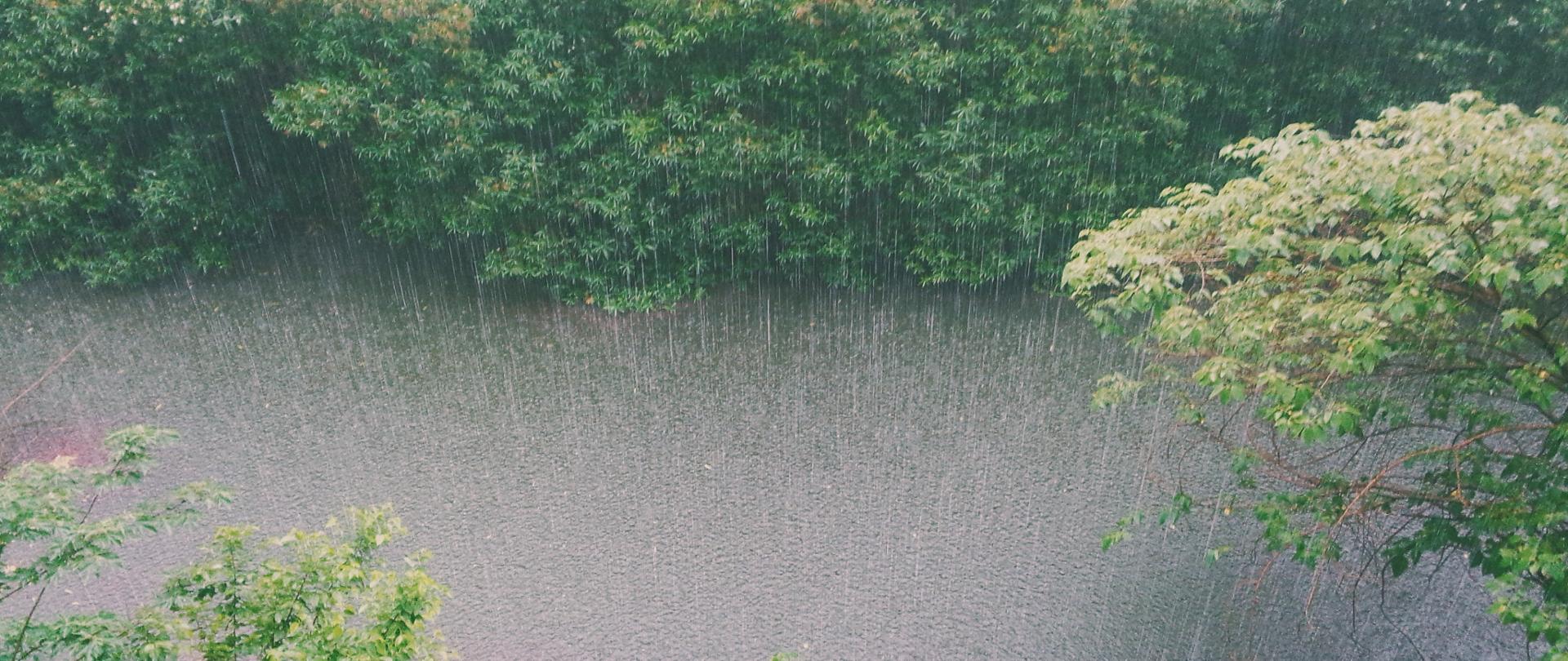 Zdjęcie przedstawia rzekę, nad którą bardzo intensywnie pada deszcz.
