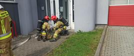 Zdjęcie przedstawia strażaków podczas ćwiczeń na terenie Jednostki Ratowniczo - Gaśniczej Nr 1 w Koninie. Strażacy na zdjęciu przed budynkiem. 