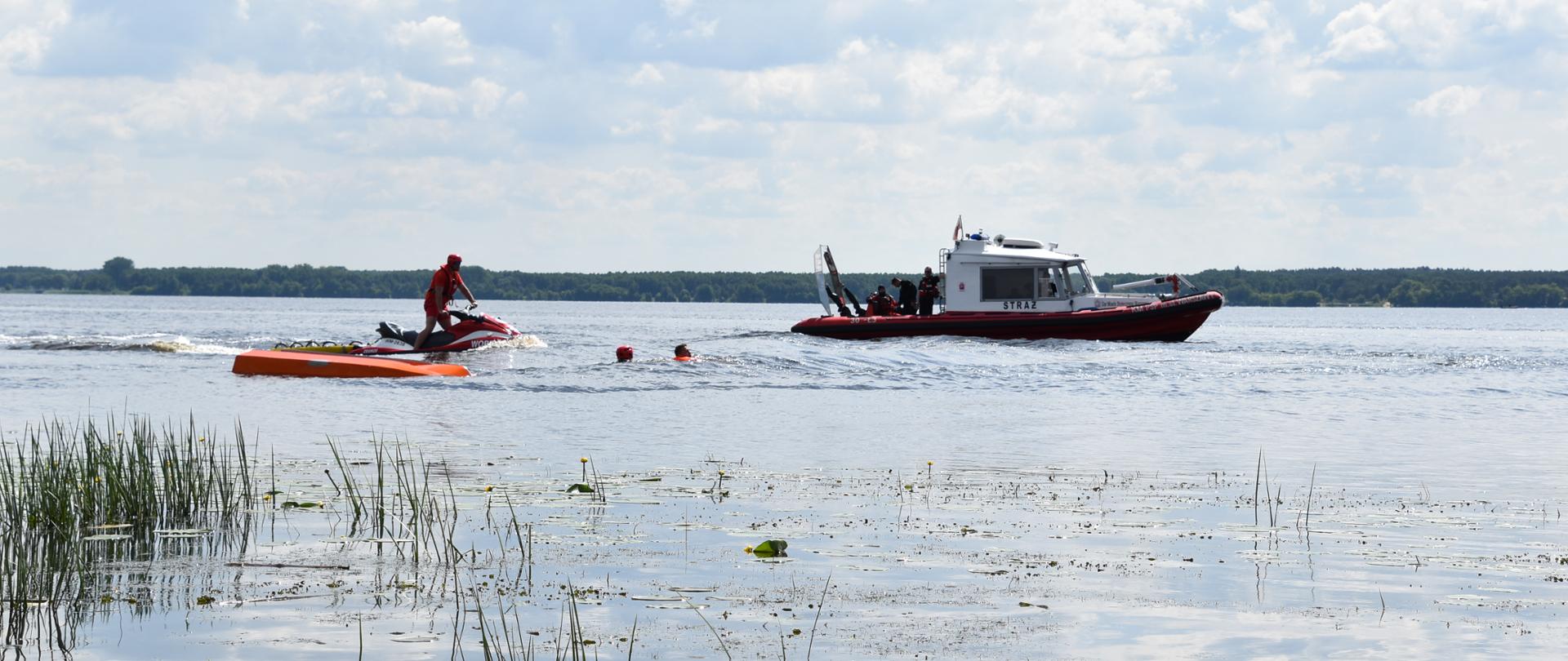 ratownicy wodni na jeziorze - jeden na skuterze, kilku w łodzi motorowej płynący do dwóch osób w wodzie