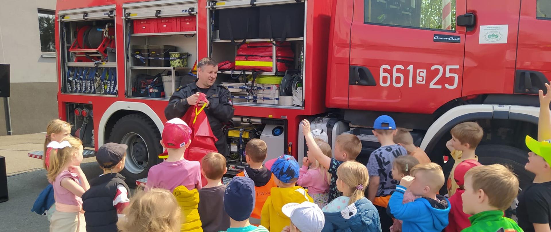 Na zdjęciu strażak pokazuje dzieciom sprzęt strażacki z samochodu pożarniczego