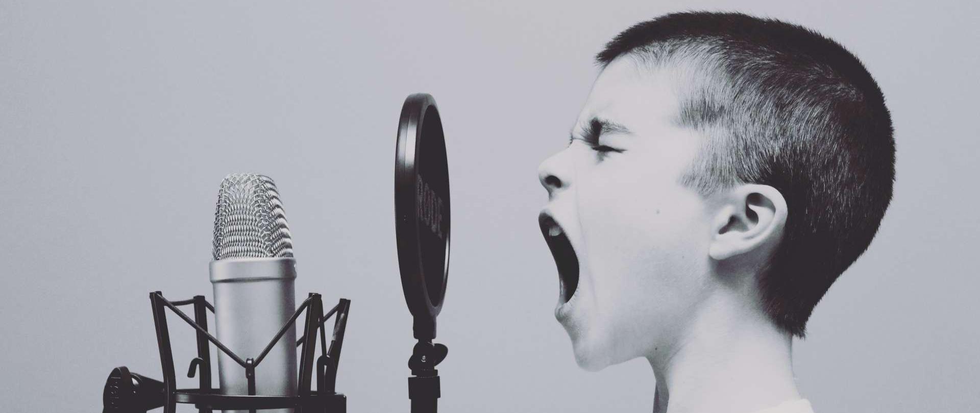 zdjęcie przedstawia chłopca śpiewającego do mikrofonu studyjnego