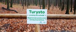 Zdjęcie przedstawia drewnianą barierę na tle lasu, na barierze tabliczka z napisem: "Turysto, prosimy nie wchodź! Regeneracja powierzchni cennej przyrodniczo" 