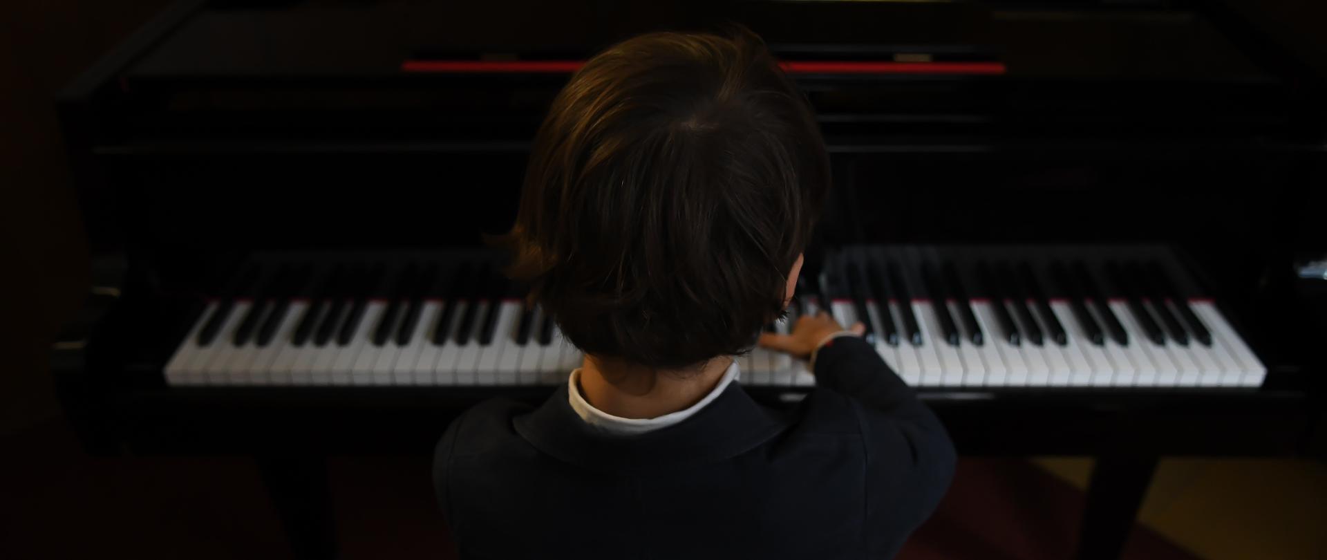 zdjęcie przedstawiające ciemnowłosego chłopca siedzącego przy fortepianie