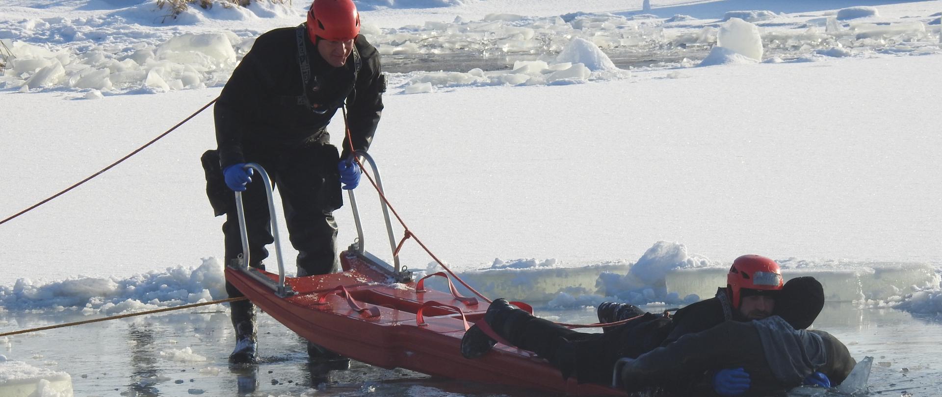 Wykorzystanie sań lodowych - sprzętu w dyspozycji strażaków do wyciągnięcia człowieka, pod którym załamał się lód z wody