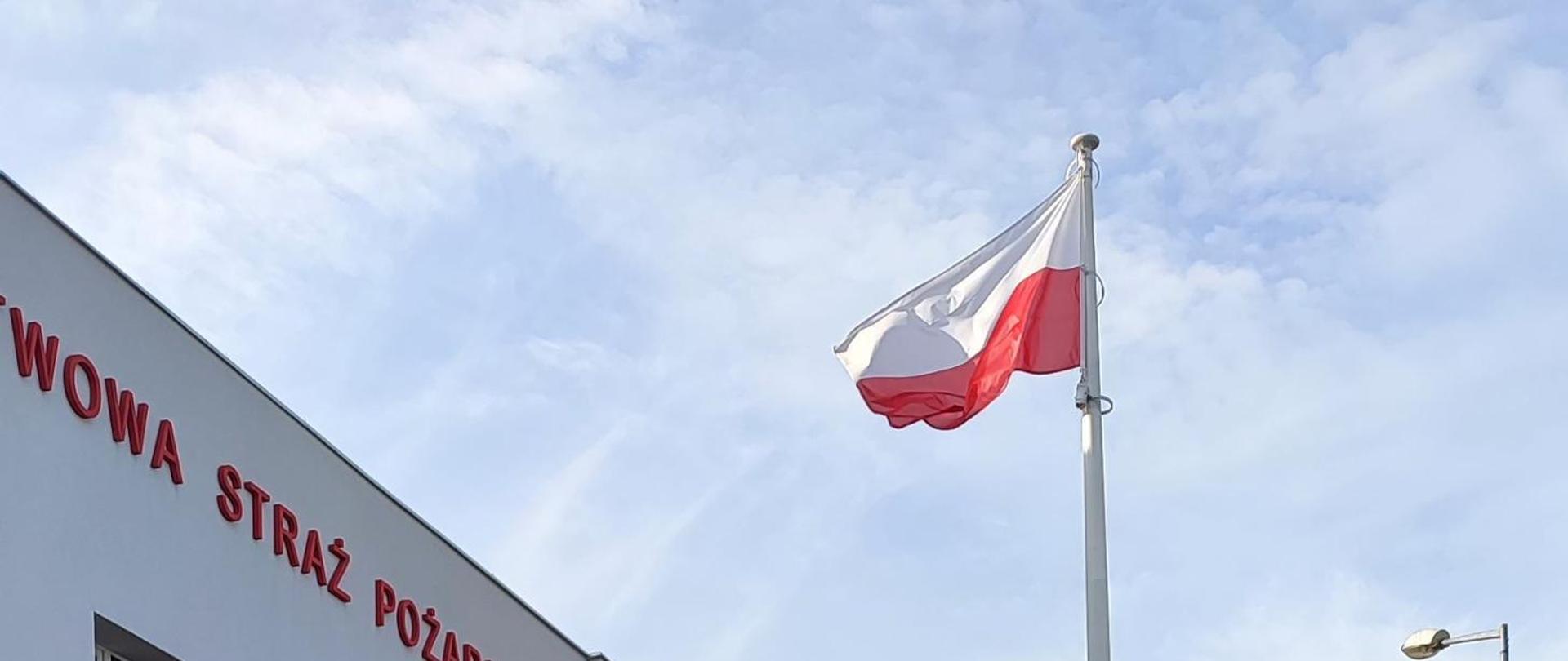 Na zdjęciu widnieje Flaga Rzeczypospolitej Polskiej na maszcie, w tle niebo.