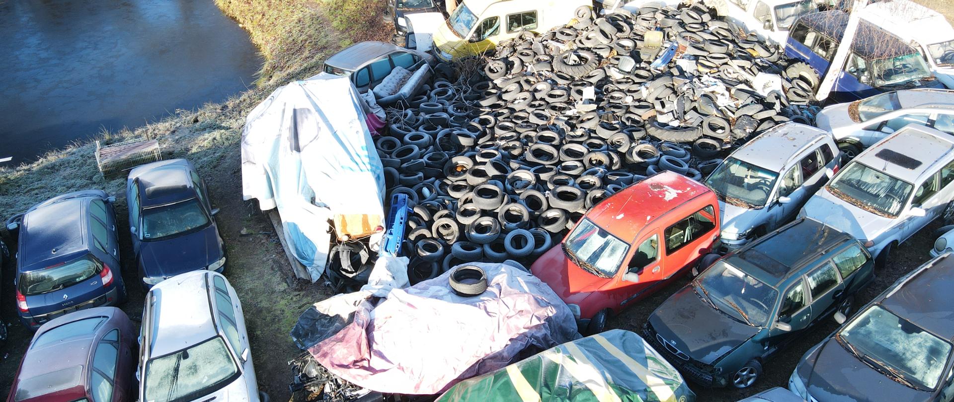 Widok z góry na zgromadzone odpady w postaci zdemontowanych w różnym stopniu pojazdów i zużytych opon 