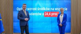 Minister Wieczorek i wiceminister Mrówczyńska stoją na sali, za nimi na wbudowanym w ścianę wielkim ekranie napis Ogólny wzrost środków na wsparcie studentów o 24,4 proc.